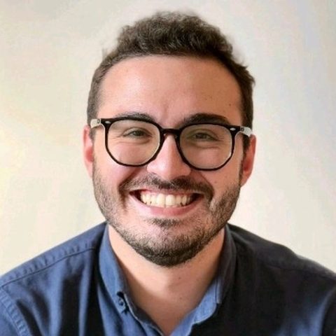 Artur Batissoco, fundador do FaixaDeObra, sorrindo, de óculos e camisa azul